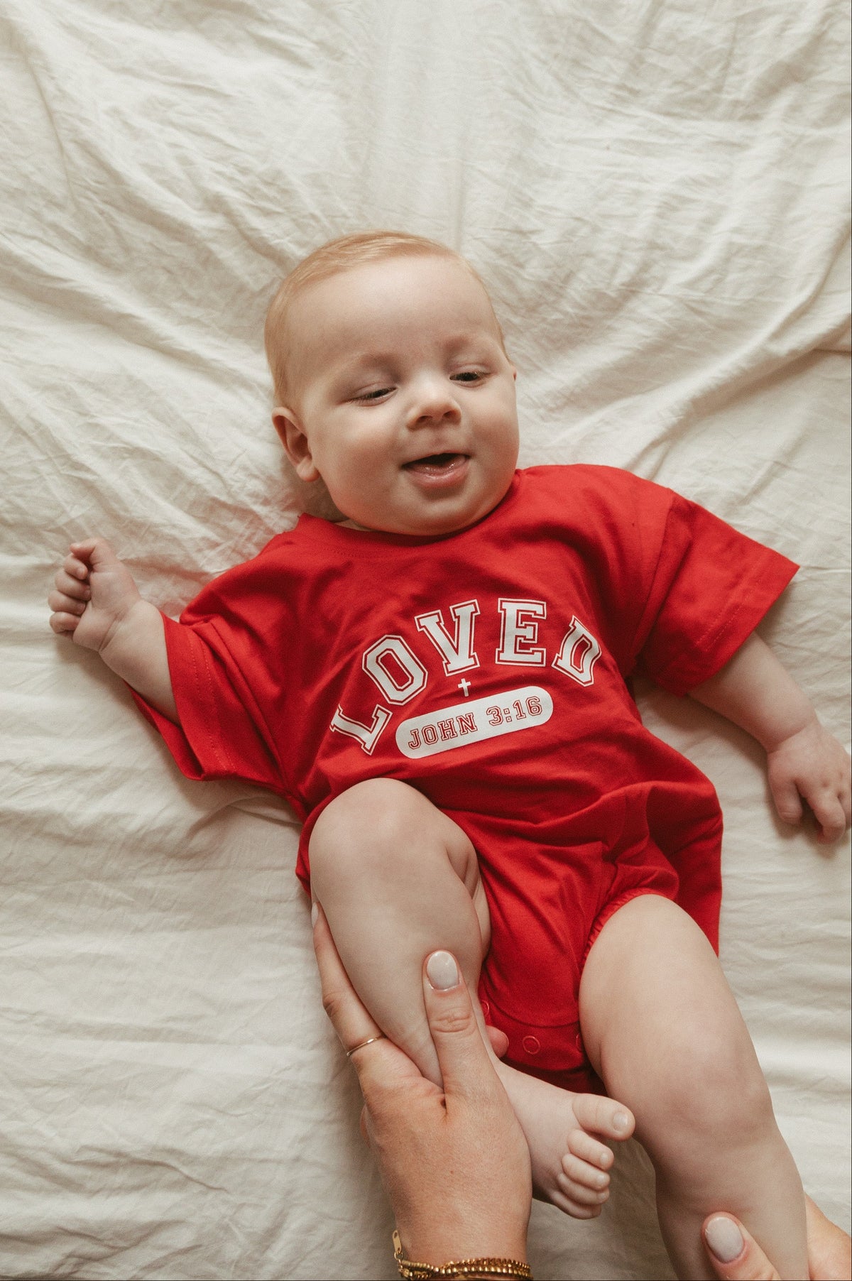 Baby wearing a red 'LOVED' onesie lying on a white blanket